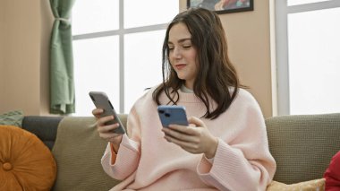 Genç bir kadın, rahat bir oturma odasındaki koltukta otururken akıllı telefonları karşılaştırıyor, tercihlerini ve teknolojilerini ifade ediyor..