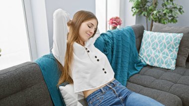 Rahat genç bir kadın, rahat, modern bir apartman dairesinde, rahat bir kanepede uzanıyor, gündelik güzellik ve rahatlığı somutlaştırıyor..