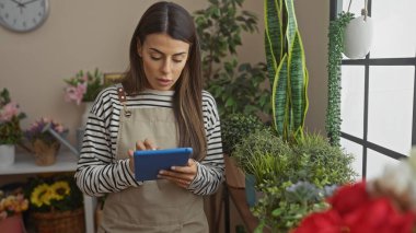 Bitkilerle çevrili rahat bir evde tablet kullanan konsantre genç bir kadın.