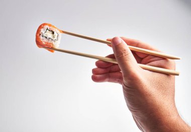 Bir adamın eli yemek çubuklarıyla suşiyi zarif bir şekilde temiz bir zemin üzerinde tutar. Mutfağı ve hassasiyeti vurgular..