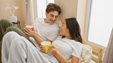 Sıcak bir yatak odasında kahvesini yudumlayan, sıcaklığı ve samimiyeti çağrıştıran neşeli ırklar arası bir çift..