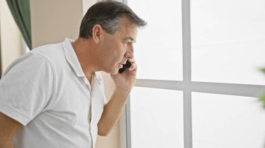 Akıllı telefondan konuşan olgun bir adam pencereden dışarı bakar. Bir iletişim ve yansıma anı tasvir eder..