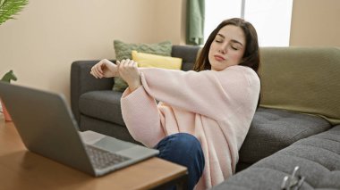 Genç bir kadın rahat bir evde dizüstü bilgisayarını kullanmaya ara verirken esniyor..