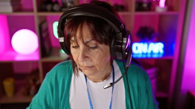 Renkli bir oyun odasında kulaklık takan olgun bir kadın geceleri bilgisayar oyununa konsantre oluyor..