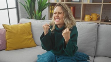 Neşeli genç bir kadın, keyifli bir anı kutluyor. Gri bir kanepede, rahat bir oturma odasında..