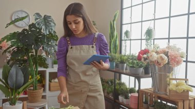 Parlak bir çiçekçinin içindeki çeşitli bitkiler arasında tabletle çalışan İspanyol kadın.