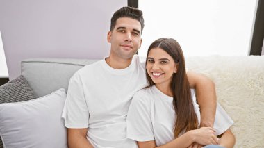 Gülümseyen bir kadın ve bir adam modern bir oturma odasında bir kanepeye kıvrılmış sevgi ve mutluluk yayıyorlar..