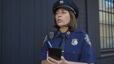 Olgun bir kadın polis memuru, şehir sokağında dururken not defterine not alıyor..