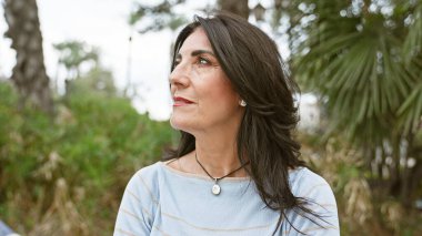 Olgun İspanyol kadın yeşil yapraklı sakin bir parkta dalgın dalgın dalgın bakıyor.