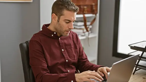 stock image Hispanic businessman typing on a laptop in a modern office, showcasing professionalism and concentration.