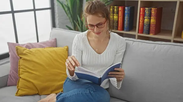 在舒适的家客厅里看书的白人女人 图库图片