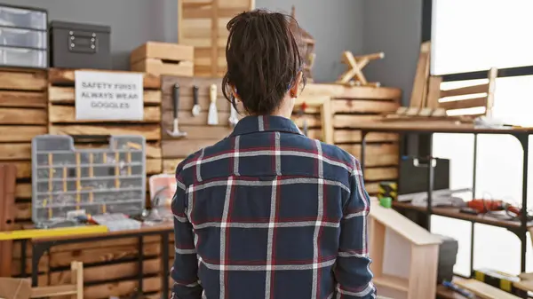 一位穿着格子呢衣服的妇女在一间设备齐全的木工车间里苦思冥想地站着 代表着木工的专业精神 免版税图库照片