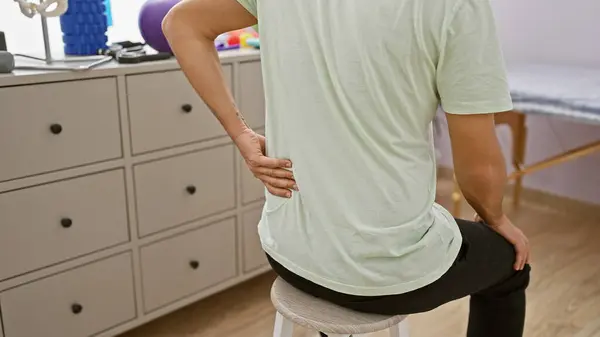 Young Man Rehab Clinic Holds His Back Suggesting Pain Clinical Stock Image
