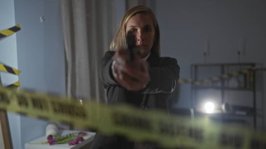 Ciddi bir kadın dedektif suç mahalli odasına uyarı bandı ve kanıtlarla silah doğrultuyor..