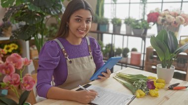 Çiçekçide notlar alan İspanyol bir kadın. Etrafı renkli buketler ve bitkilerle çevrili..