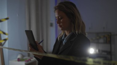 Odaklanmış genç bir kadın dedektif, gece vakti suç mahallinde cep telefonu ve kalemiyle kanıtları inceliyor..