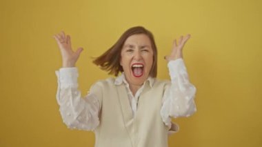 Heyecanlı orta yaşlı İspanyol kadın, kazanan kollarını kaldırmış kızgın, izole edilmiş sarı arka plandaki başarısını kutluyor.