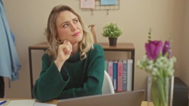 Sıcak bir evde dizüstü bilgisayar kullanan gülümseyen genç sarışın bir kadın, rahat ve profesyonelce davranıyor..