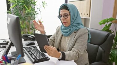 Türbanlı profesyonel bir kadın modern bir ofiste tableti inceleyerek deneyim ve odaklanma sağlar..