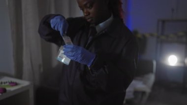 Afrika kökenli Amerikalı kadın dedektif, kapalı mekan suç mahallindeki kanıtları rozet aydınlatma oturma odasıyla analiz ediyor.
