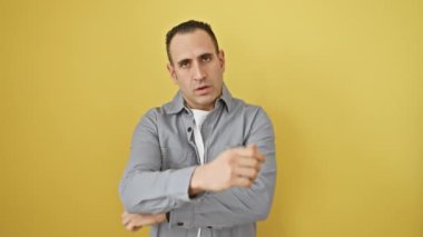 Yorgun, tişörtlü, yorgunluktan bitap düşmüş, yorgun gözleri ve burnu ovuşturan, baş ağrısıyla boğuşan genç bir İspanyol. Sarı izole arka planda gerginlik, hayal kırıklığı ve baskı ifade eder.