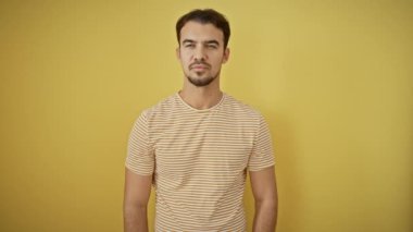 Şaşırmış genç, sakallı, şaşkın bir şekilde ayakta duran, ağzı korkuyla dona kalmış, çizgili bir tişört giymiş, tek başına sarı bir arka planda duran bir İspanyol. Şaşırmış bir adamın duygu dolu portresi.