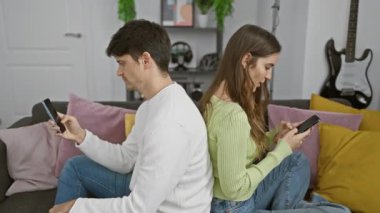 Sırt sırta verip, rahat, modern bir oturma odasında akıllı telefonlarına sarılmış bir kadın ve erkek..
