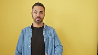 Kot gömlekli, ağzı açık, şaşırmış genç İspanyol adam! Neşeli bir şekilde, canlı sarı bir arka planda yan tarafı işaret ediyor.!