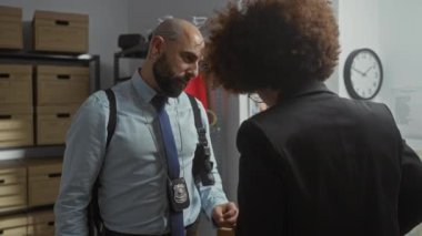Ofiste rozetli bir adam ve bir kadın dosya dolapları ve bir duvar haritasıyla bir davayı tartışıyorlar..