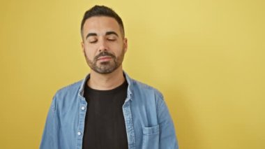 Mutluluktan uçuyor, kot gömlek giyen genç İspanyol adam, kocaman gülümsüyor, başparmağını kaldırıp yan tarafı işaret ediyor. Reklam programınız için mükemmel izole edilmiş sarı arkaplan