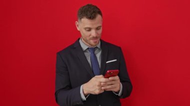 Takım elbiseli genç bir İspanyol, izole edilmiş, kırmızı bir arka planda kameraya sevgi dolu bir öpücük yolluyor. Aşkı teknoloji ile ifade etmek, akıllı telefondaki seksi, sevimli ifade