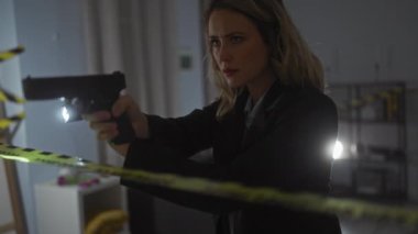 Takım elbiseli sarışın kadın dedektif dikkatli bir bantla silahı içeri doğrultuyor.
