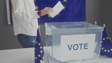 Bir kadın oy pusulasını eu bayraklarıyla süslenmiş bir Avrupa seçim ofisinde kullanıyor.