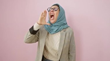 Orta yaşlı tesettürlü İspanyol kadın güçlü çığlıklar atıyor! Ağzını kapatır, yana doğru yüksek sesle bağırır izole edilmiş pembe bir arka planda hayal kırıklığıyla iletişim kurar..