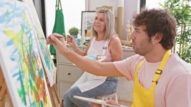 İki kendine güvenen sanatçı, erkek ve kadın, kapalı alan sanat stüdyosunda resim yaparken, birlikte resim çizmekten zevk alırlar.