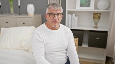 Omg! Şok olmuş orta yaşlı, gri saçlı, pijamalı bir adam şaşırmış bir ifade ve yatak odasında bir onay sembolü sergiliyor..