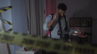 Odaklanmış bir İspanyol dedektif telefonda konuşurken loş ışıkta yanan bir suç mahallini araştırıyor..