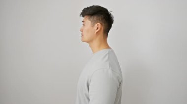 Kendine güveni tam genç bir Çinli yan görüş profilinde rahatça poz veriyor. Tişört giyer, doğal yüzüne güven veren bir gülümseme takınır. beyaz arkaplanda izole.