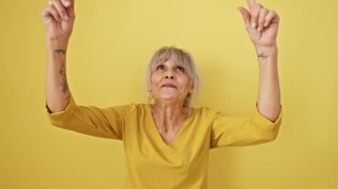 Midilli kuyruklu neşeli orta yaşlı kadın, şaşkınlık ve şaşkınlıkla dolu, işaret ediyor, izole edilmiş sarı duvarın üzerinden pozitif enerji saçıyor. Olgun ve mutlu hayatının tadını çıkarıyor.!