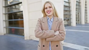 Kendine güvenen, şık, genç, sarışın bir kadın şehir ortamında poz veriyor. Palto giyiyor, zarafet saçıyor..