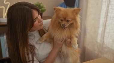 Hoş bir oturma odasında sevimli bir Pomeranian köpeği tutan mutlu genç bir kadın.