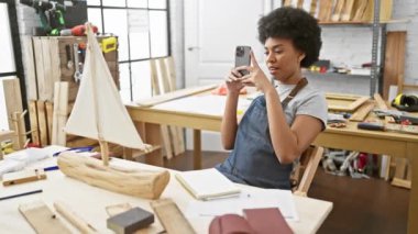 Afrika kökenli Amerikalı bir kadın güneş ışığında marangozluk atölyesinde gemi modeli yakalıyor.