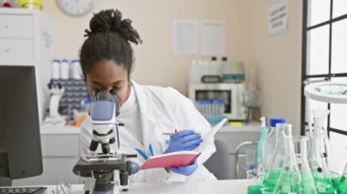 Mikroskopla gözlemleyen ve laboratuarda notlar alan Afrikalı kadın bilim adamı.