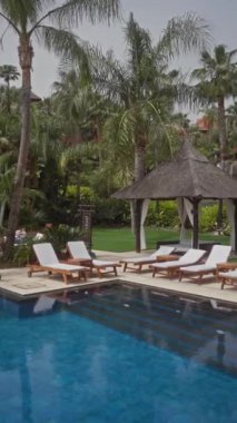 Havuzu, kulübesi, güneşli yatakları, palmiyeleri ve bulutlu bir tatil merkezinde lüks bahçesi olan tropik bir tatil yeri..