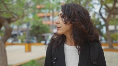 Şehir parkında gülümseyen esmer, kendinden emin orta yaşlı bir kadının portresi..