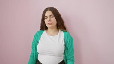 Endişeli genç kadın kol saatindeki zamanı kontrol ediyor, geç kalmaktan korkuyor, pembe arka planda tek başına duruyor.