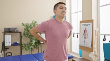 Bir rehabilitasyon kliniğinde sırt ağrısı çeken İspanyol bir adam. Tedavi yatağı ve anatomik posterlerin yanında..