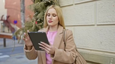 Sarışın kadın şehir sokaklarında tablet kullanıyor, selfie çekiyor, gülümsüyor, kentsel geçmişi ve şenlikli dekorasyonu var..