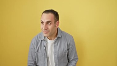 Tişörtlü, gülümseyen ve mesafeyi arayan mutlu İspanyol genç adam. Sarı arka planda izole edilmiş, el koruyucu gözlerle tek başına dikiliyorsun..