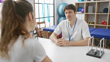 Erkek bir fizyoterapist, iyi donanımlı bir fizyoterapi kliniğinde kadın bir hastaya danışmanlık yapıyor..